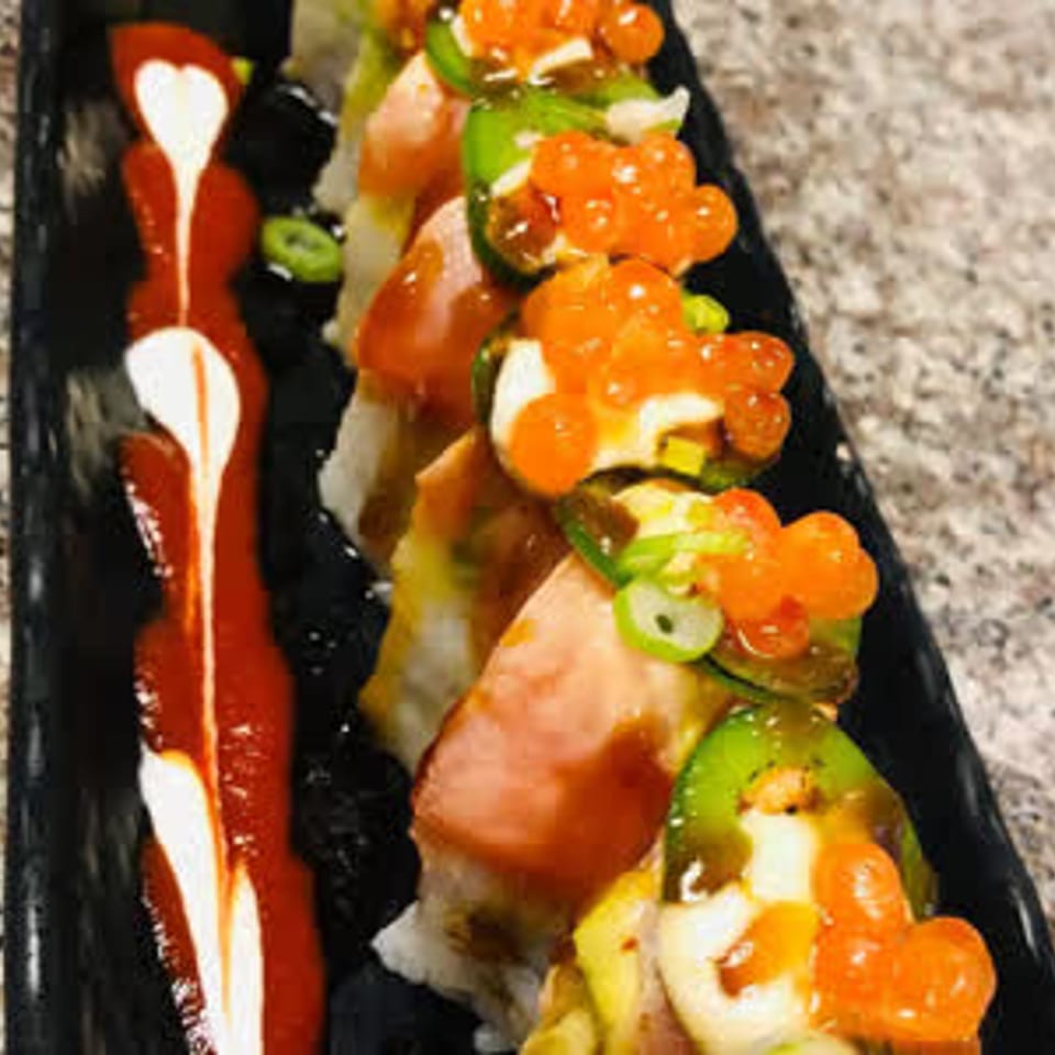 Sushi roll topped with roe and scallions on a black plate