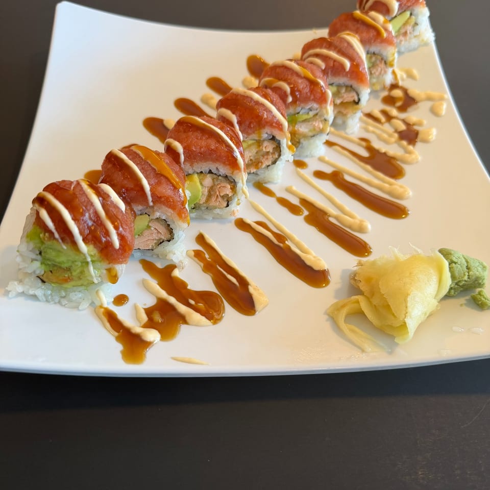 Sushi roll drizzled with sauces on a white plate with ginger and wasabi