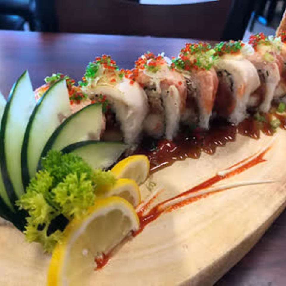 Sushi roll on a wooden serving board with cucumber and lemon